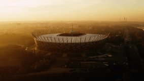 Aerial drone shot of PGE Narodowy national stadium in Warsaw city backlit with warm sunrise sun light, beautiful misty autumn morning, sunny dusk dawn orange colour, cityscape - Powered by Shutterstock - Get 15% off with code: PIKWIZARD15