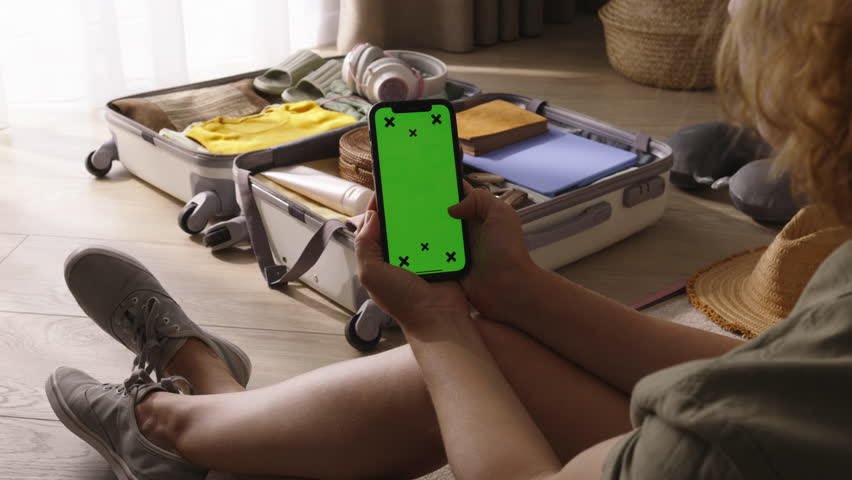 Woman with phone green chromakey screen. Woman after long nice vacation near open baggage suitcase swaps photos from trip nostalgic watching memorable photos taken on vacation. Warm nostalgic feelings Royalty-Free Stock Footage #1108949709