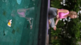 Frangipani flowers floating in the swimming pool and mid adult woman doing yoga at background, outdoors shot - Powered by Shutterstock - Get 15% off with code: PIKWIZARD15