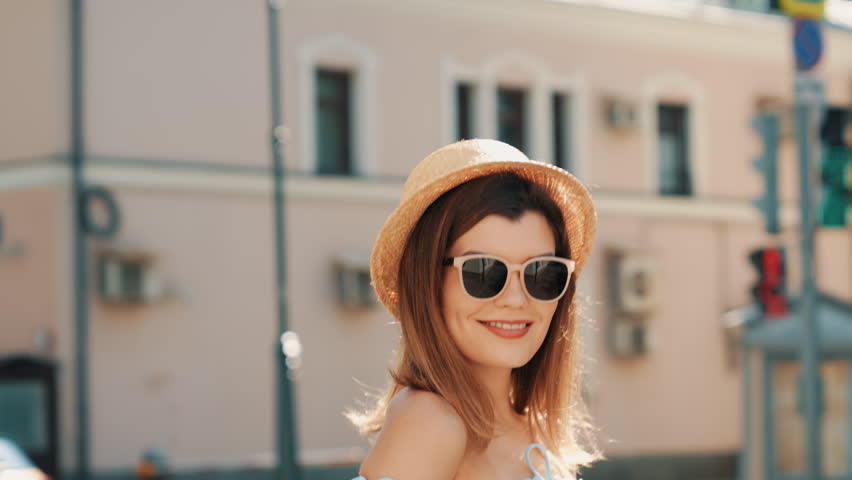 Young beautiful smiling hipster woman in trendy summer clothes. Carefree model posing in the street at sunny day. Positive brunette female outdoors. Cheerful and happy. In hat and sunglasses Royalty-Free Stock Footage #1108951113