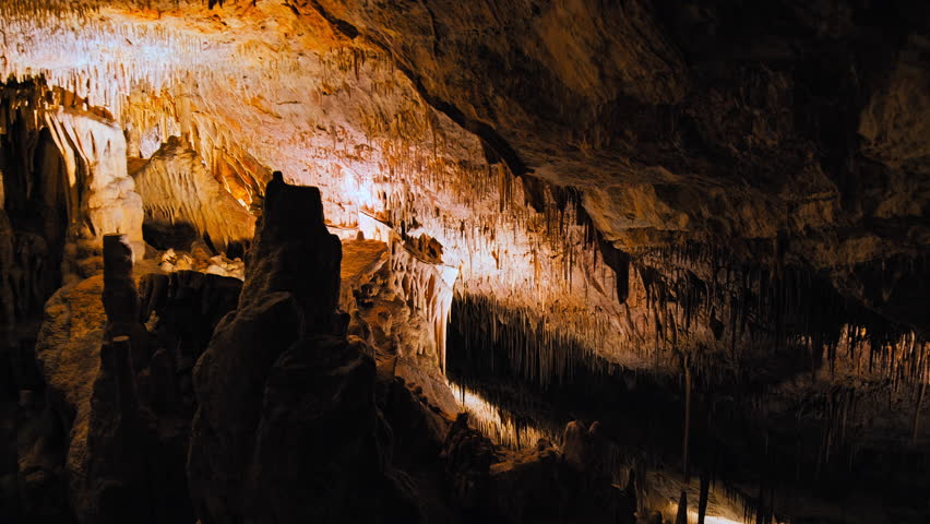 An underground cave formed of carbonate limestone rocks in Majorca, Spain. A colourful natural scenery in a cave with ancient cavities of stalactites and stalagmites on Mallorca, Balearic Islands. Royalty-Free Stock Footage #1108956561