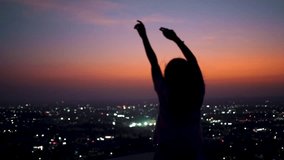 Teenager girl rising her hands on the sunset at a top of the hill with city silhouette on the background. Female tourist enjoying city view during night.  - Powered by Shutterstock - Get 15% off with code: PIKWIZARD15