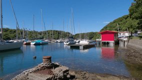 A view of a yacht harbor in an inlet surrounded by mountains. The contrast between the blue sky and the red hut is striking in this video.