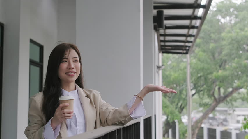 Satisfied businesswoman holding takeaway coffee on office balcony and catching raindrops