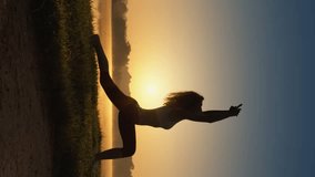 Silhouette of slender woman at sunrise vertical video. Practicing yoga to increase energy and vitality. Mind and body in harmony: outdoor yoga dividing the pond. Breathtakingly beautiful body figure