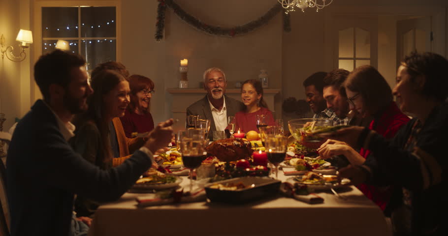 Diverse Group of Relatives and Friends Sitting Together Behind a Dining Table with Tasty Meals and Festive Winter Decorations. Big Happy Family Having Fun conversation, Enjoying a Holiday Evening