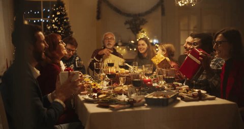 Snowy House Window Footage: Diverse Family Exchanging Christmas Gifts to Celebrate Christmas. Beautiful Old and Young Relatives Excited to Receive Presents. Holiday Dinner Together at Home Stock Video
