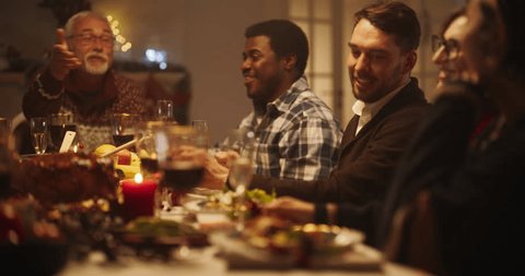 Diverse Group of Relatives and Friends Sitting Together Behind a Dining Table with Tasty Meals and Merry Winter Decorations. Big Happy Family Having Fun conversation, Enjoying a Holiday Evening Stock Video