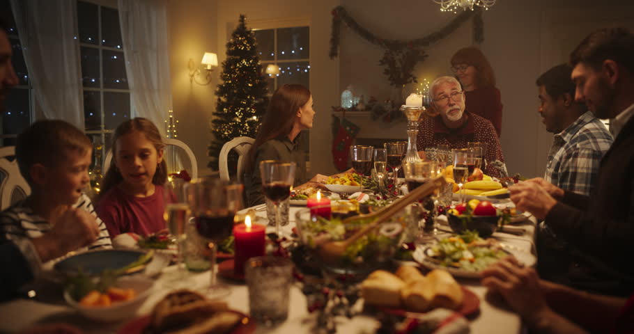 Multicultural Group of Close Friends and Family Members Enjoy a Christmas Turkey Dinner, Spending Holiday Season Together. Festive Evening Atmosphere, Decorations with Christmas Tree at Home Royalty-Free Stock Footage #1108965049