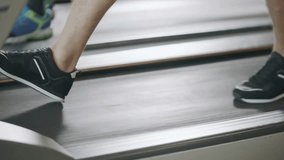 Closeup of male feet in sneakers training and walking on incline treadmill view on sportsman exercising and jogging on running machine at gym