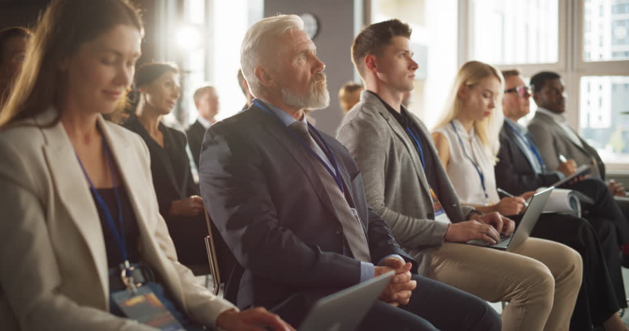 Senior Caucasian Male Entrepreneur Sitting In Diverse Crowd On Business Forum. Successful Investor Listening To Presenter Pitching Startup Idea On Stage. Businessman Attending Technology Conference. Royalty-Free Stock Footage #1108971053