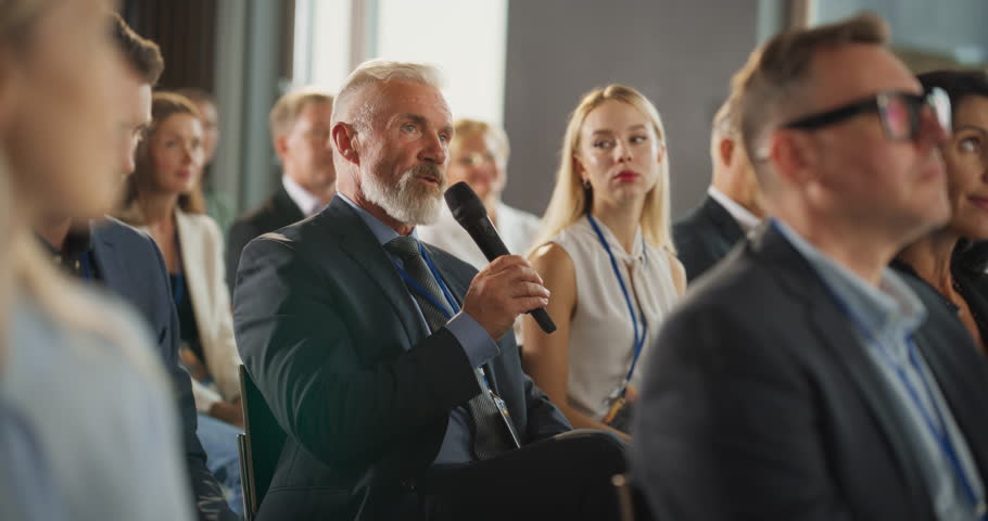 Senior Male Investor Sitting In Crowd And Using Microphone To Ask A Question At International Technology Conference. Caucasian Man Listening To Keynote Presentation About New Startup Company Service. Royalty-Free Stock Footage #1108971065