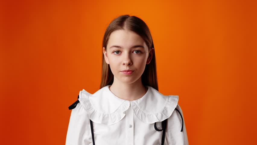 Smiling teen girl waving hello greeting against orange background in studio
