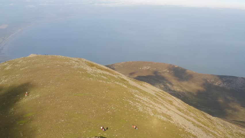 Cinematic aerial at Slieve Donard peak. Camera tilts up revealing