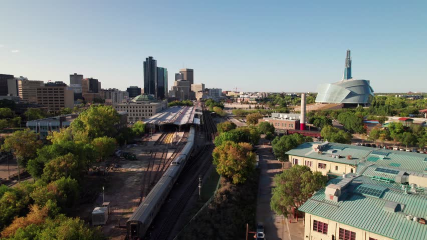 Aerial of Via Rail train entering Union Station in Winnipeg, MB. Human Rights Museum and Forks Market visible, 4K drone shot