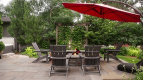 static shot of a propane fire pit surrounded by Adirondack chairs with a large red umbrella on a patio during the day - Powered by Shutterstock - Get 15% off with code: PIKWIZARD15