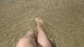 Bare female legs on the seashore are washed by small waves