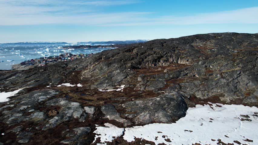 Small township behind rocky hill in Greenland, aerial drone view