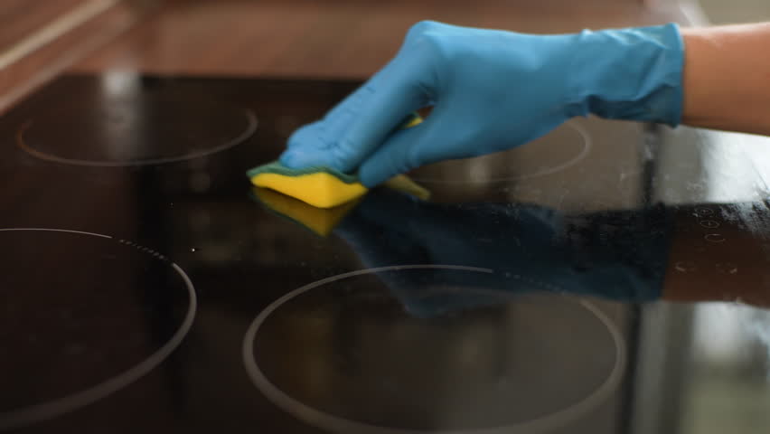 Close-up cropped shot of unrecognizable housewife cleaning induction stove in kitchen. Closeup of young man in rubber gloves wiping cooking top with sponge doing housework in kitchen, slow motion. | Shutterstock HD Video #1108979507