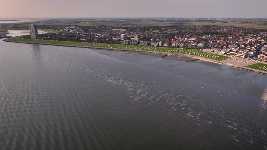 Aerial shot of the town of Büsum on the German North Sea coast with people walking Wadden Sea by low tide. Büsum, the North Sea health spa town, stretches from the Family Lagoon to the harbor. | Shutterstock HD Video #1108984037