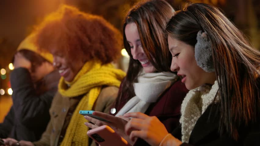 Hipster group of millennial friends using cell phones sitting together outdoor. Diverse people looking social media content on smart phone devices in city street. | Shutterstock HD Video #1108984317