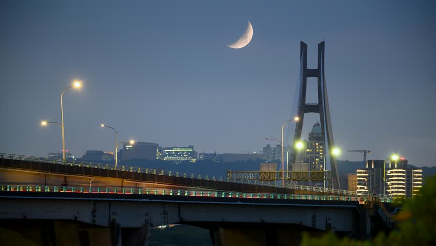 There is a steady stream of vehicles on the bridge. Half moon and New Taipei Bridge at night, Taiwan.