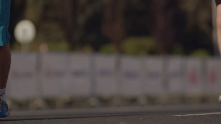 Close-up view from the ground, from the side a crowd of running people in sports clothes on the asphalt on a sunny day. People participate in a race, a marathon around the city