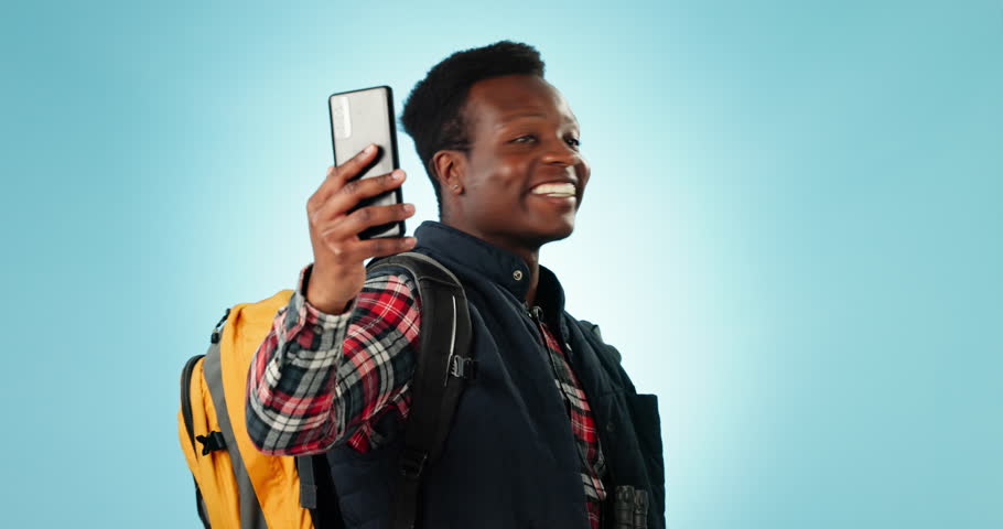 Hiking, video call and black man with backpack in studio for travel, adventure and freedom on blue background. Smartphone, conversation and guy backpacking influencer with social media live streaming | Shutterstock HD Video #1108989567