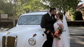 Happy laughing newlyweds admiring each other, standing near white wedding retro car. Bride in long train wedding gown talking to bearded dark-haired groom. High quality 4k footage - Powered by Shutterstock - Get 15% off with code: PIKWIZARD15