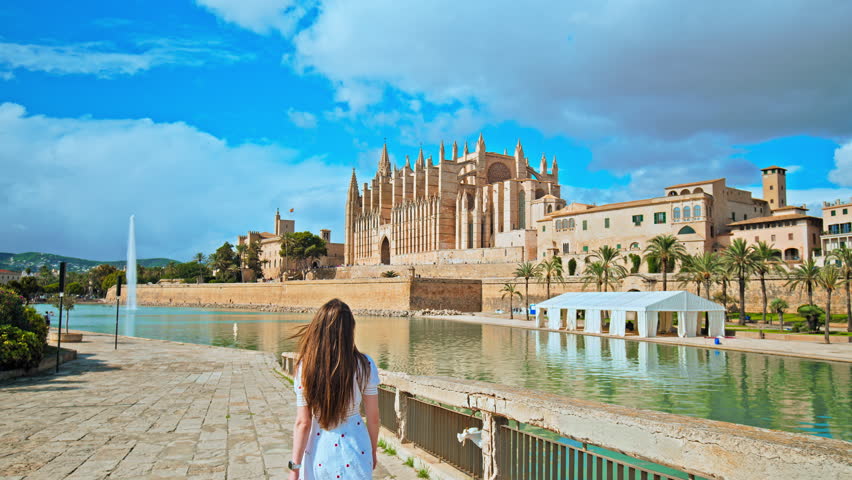 Beautiful girl tourist walking by iconic landmark in Palma Capital of Majorca. A female exploring Catedral de Mallorca and Spanish architecture in Mallorca, Balearic Islands, Spain