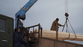 Men unload crane with wood. Clip. Workers unloading wood with crane. Crane with wooden beams is lowered into truck with worker