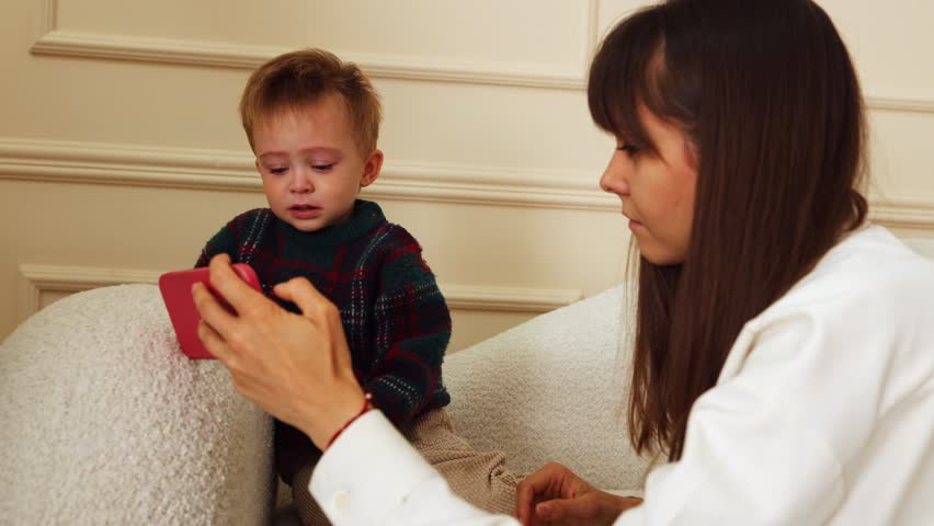 Mother shows phone to crying little son. the child watches cartoons on the phone. tears in the eyes | Shutterstock HD Video #1108997837