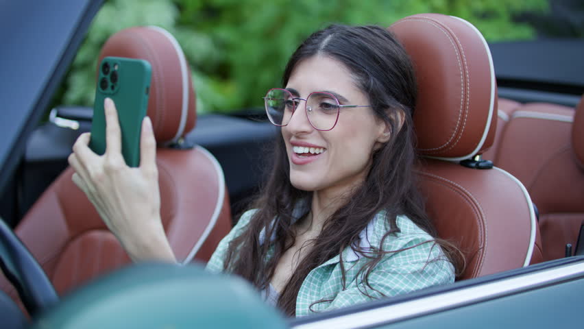 Woman is on Video Call sitting in Convertible. Female driver talking to cell phone sitting in car. | Shutterstock HD Video #1108998331