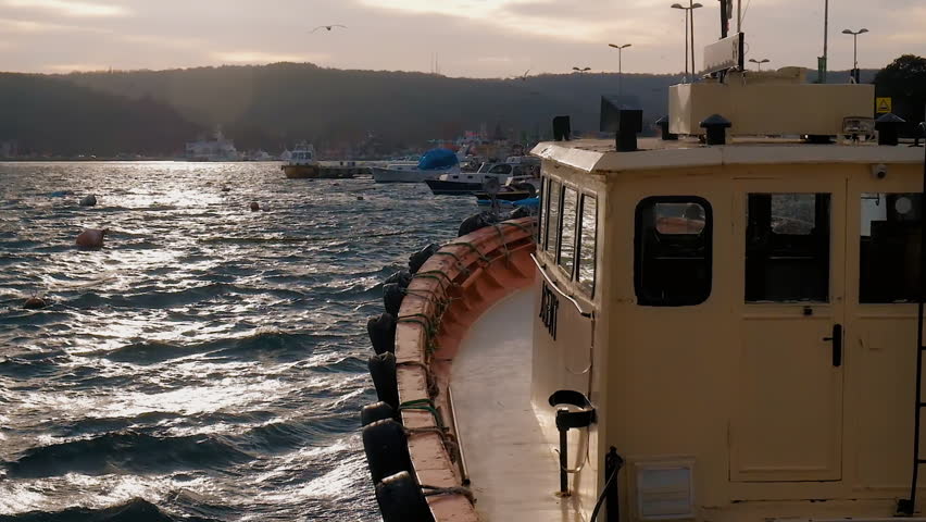 View of the waterfront at sunset with red and yellow trawler tied to the shore and swaying on the waves. Beautiful highlights on the water. Turkey, january. FullHD footage