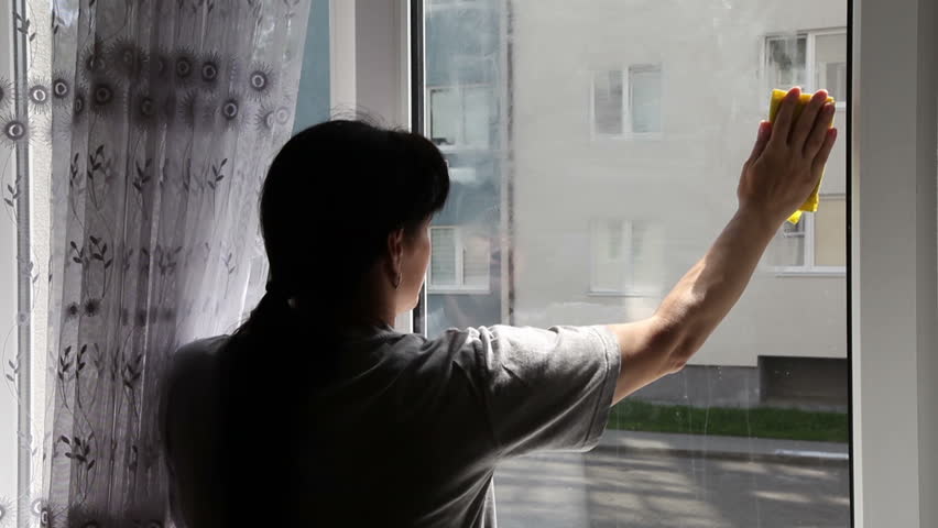 young woman in gray shirt washing the window inside