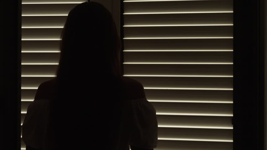 Young woman in a long dress opens her balcony doors and ventures onto the terrace, where she gracefully welcomes the mountain sunrise or sunset capturing the essence of a tranquil vacation amidst natu
