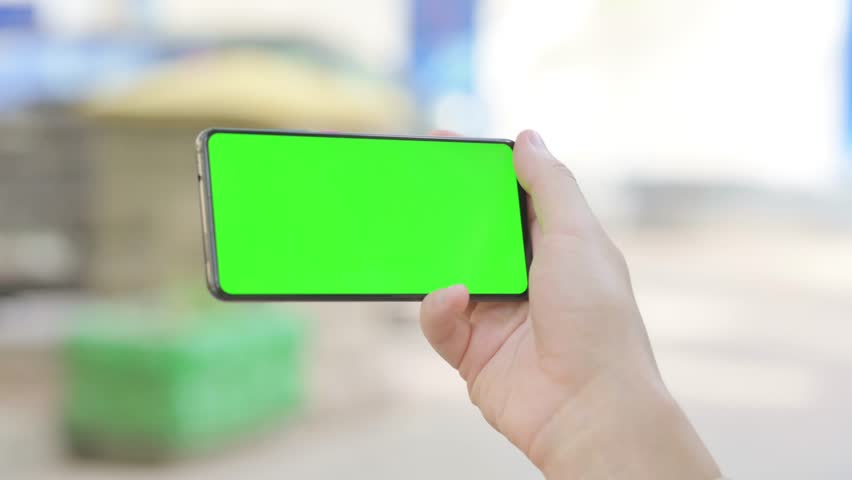 Modern Young Man Holding Phone with Green Screen Outdoor