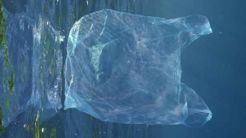Vertical video, Close-up of disposable blue plastic bag floating in blue water in bright sunshine, slow motion. Plastic pollution of Ocean, Discarded transparent blue plastic bag drifts underwater | Shutterstock HD Video #1109009043