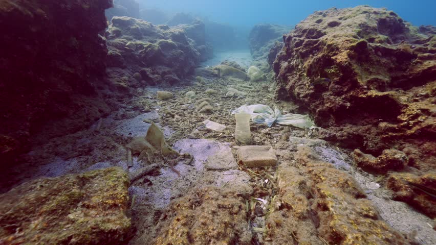 Camera moving forwards between two rocky reefs above seabed polluted with plastic trash, dead algae and other debris on blue water background, Mediterranean Sea | Shutterstock HD Video #1109009051