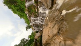 Vertical video. Dynamic FPV drone flight over a stunning waterfall close to amazing water cascades and tropical trees in the north of Thailand, in Chiang Mai province.