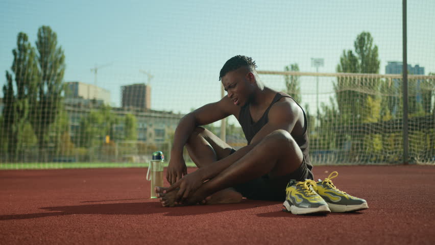African American man male runner athlete sportsman suffer from leg muscles pain feet injury painful callus on damaged foot sport trauma after run jog workout on stadium running track outdoor training Royalty-Free Stock Footage #1109014541