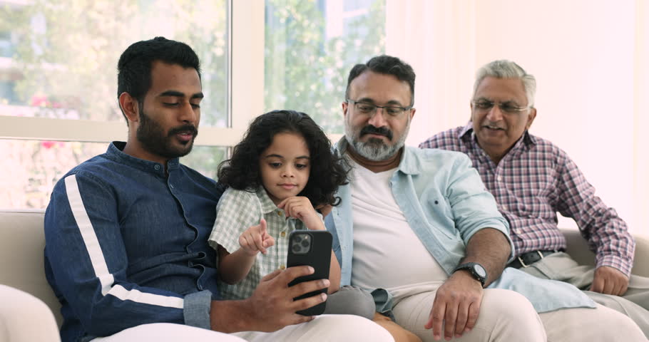 Multigenerational different age and generation Indian men and kid sit on couch having fun using smartphone. Little boy his dad, granddad, great- grandfather enjoy new mobile app on cell. Leisure, bond | Shutterstock HD Video #1109028131