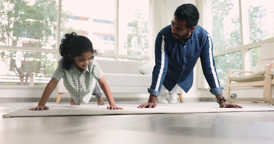 Indian father and little son doing push-up exercises at home, working out on carpet in living room. Loving dad teach preschooler kid keep healthy, sportive lifestyle, strengthen body, getting stronger