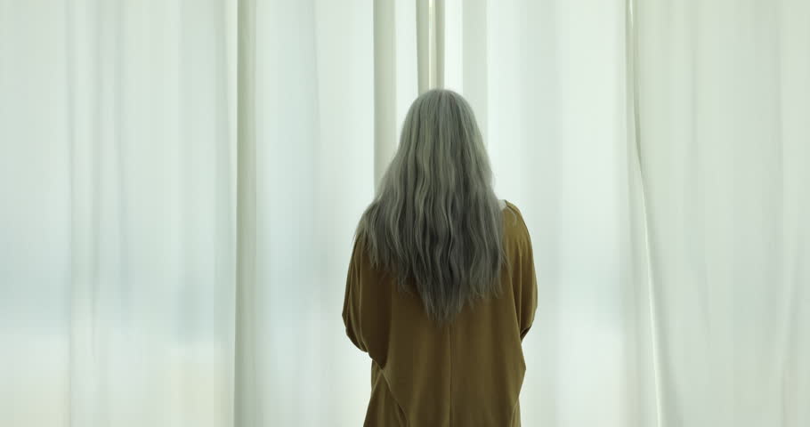 Rear view middle-aged long-haired woman standing near big window, welcoming, starting new day, opening white light curtains admiring city view from modern own apartment, enjoy vacation in modern hotel Royalty-Free Stock Footage #1109028255