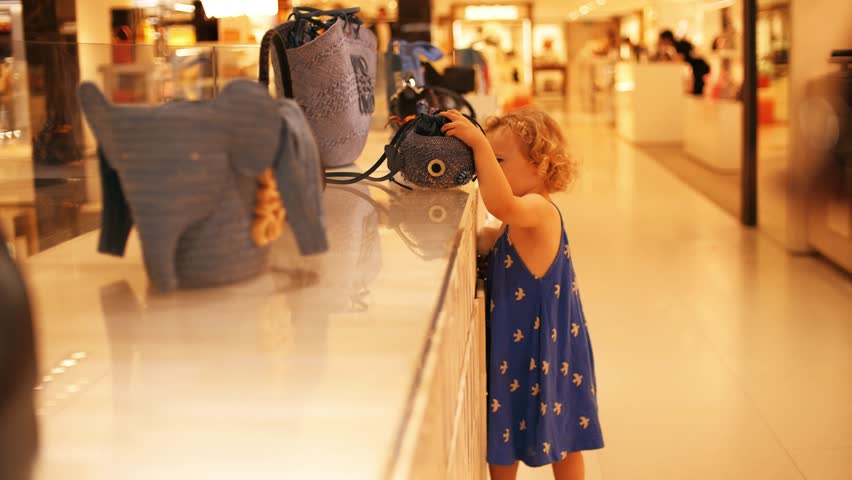 Curly little girl chooses a handbag in the shopping mall