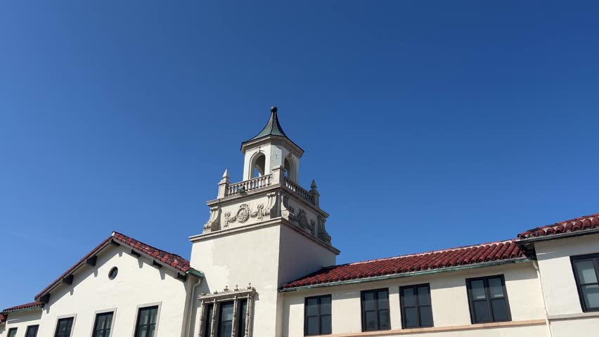 Establishing shot of a building with Spanish-style architecture against a blue sky.