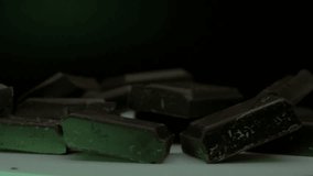 rotation of pieces of dark chocolate bar on a tray illuminated by colored lights seen close up