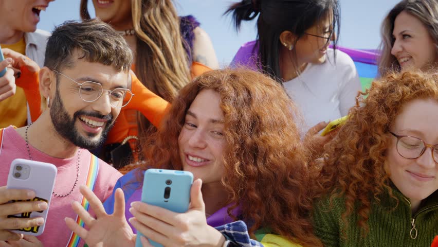 Large multiracial group young friends using cell phones outdoors. LGBT diverse community mobile addicts checking social media at gay pride festival. Generation z and crowded events in city. | Shutterstock HD Video #1109040323
