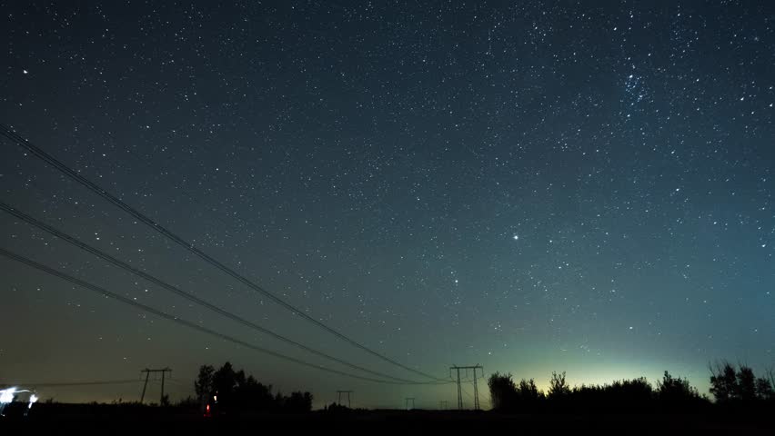 Scenery of Perseids meteor shower above field where people are standing and looking at night sky on background filmed in timelapse. Streaks of star lights painting in night heaven and leaving trail
