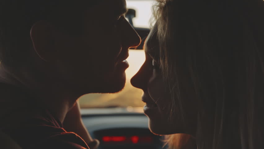 Romantic young couple kiss on the front sit of their car during the road trip. Beautiful young woman kissing her boyfriend at sunset golden light at first date. Concept of love, relations and travel. Royalty-Free Stock Footage #1109048367